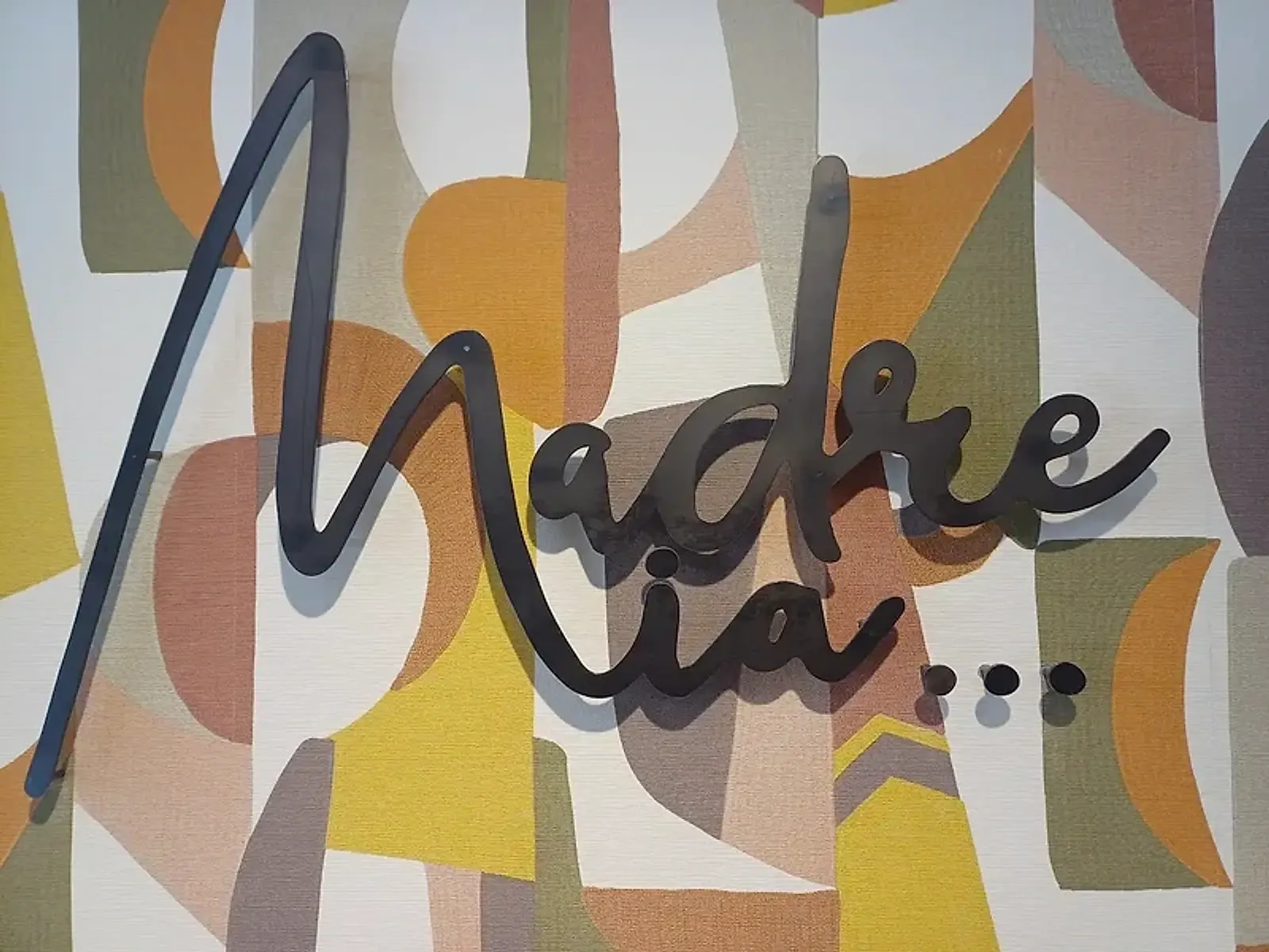 Logotipo de Madre Mía en metal sobre el mural geométrico del local